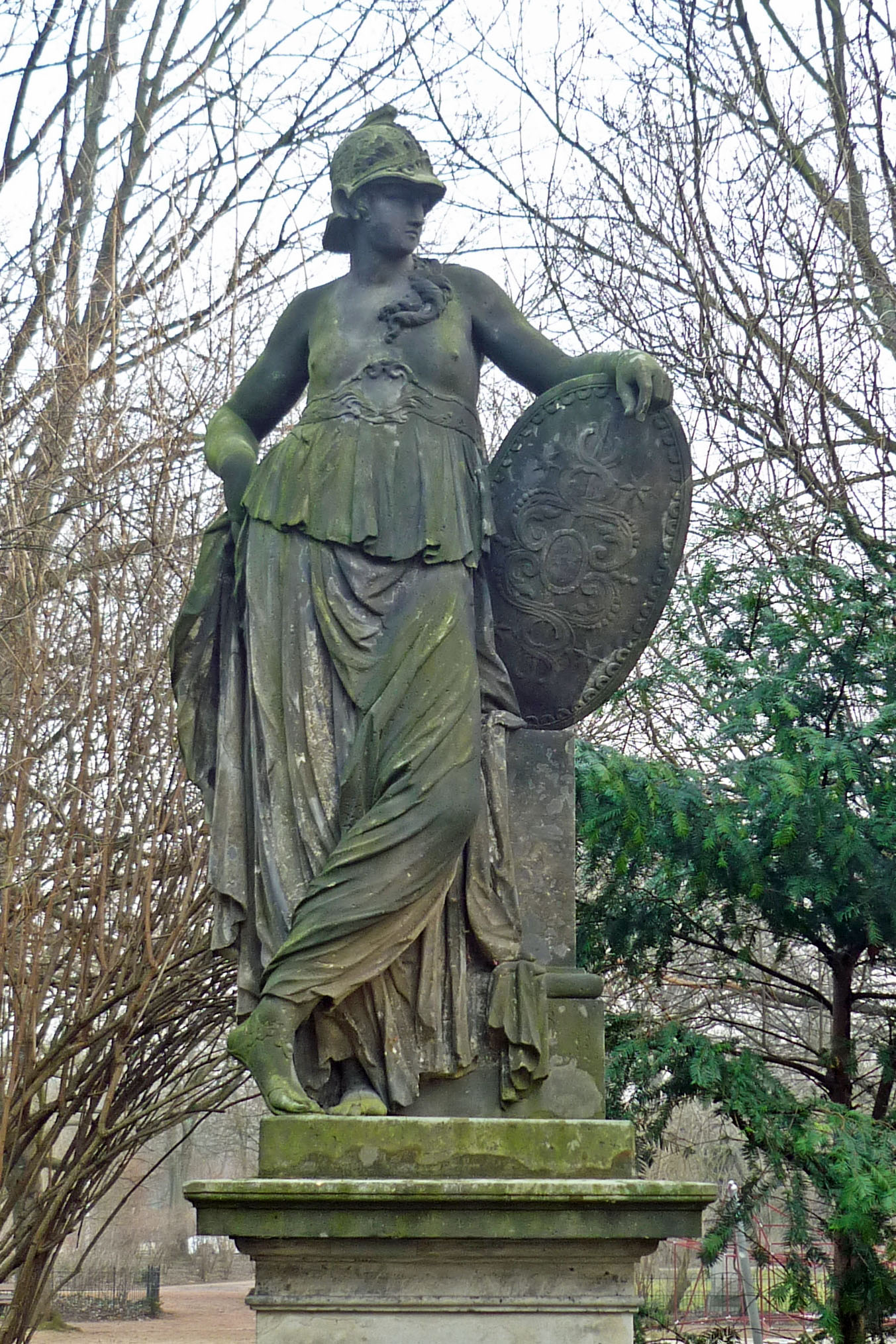 Large public sculpture of woman, bare breasted, wearing long flowing robe and helmet, leaning on a shield
