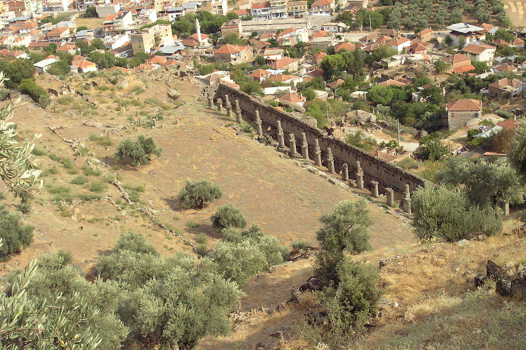 Photo of the Agora from above: ruined columns and wall, open grassy area, houses in the background